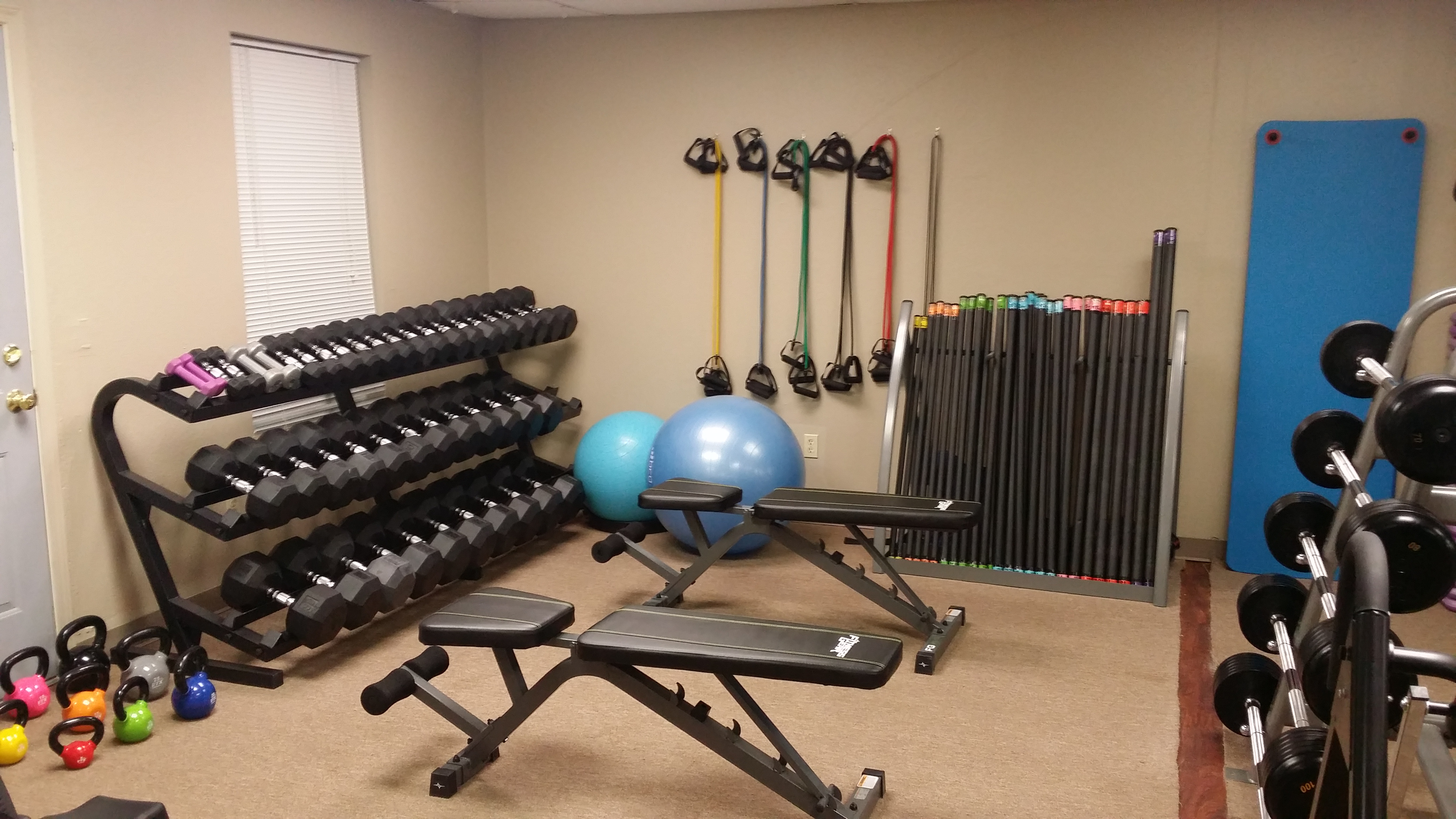 A gym with several different exercise equipment and a wall of dumbbells.