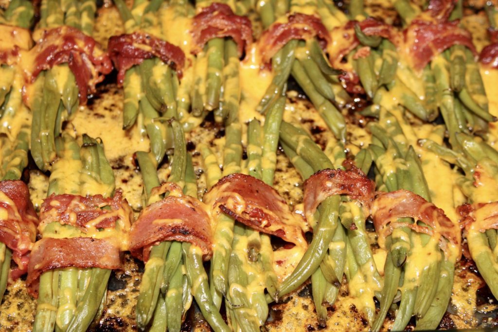 A close up of green beans covered in cheese and bacon